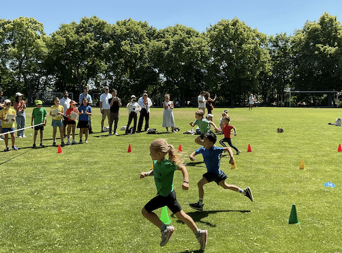 miling Key Stage 1 and EYFS students participating in a relay race on a sunny field, cheered on by House Captains from Park Lane