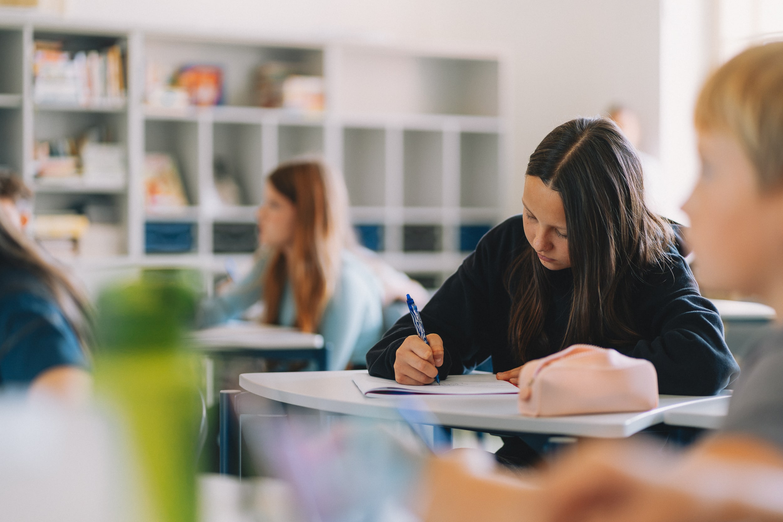 A student writing at her desk in the classroom
